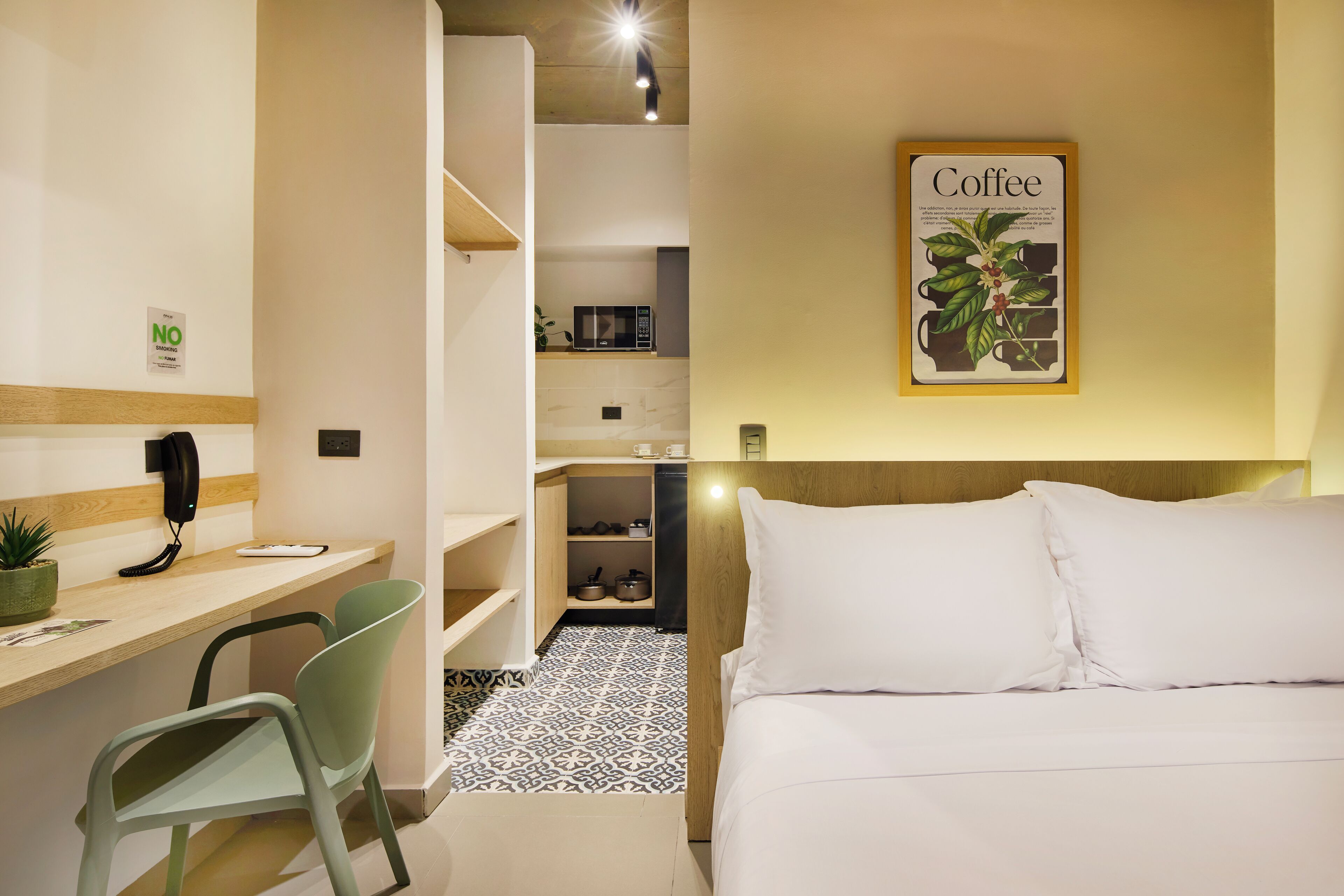 A hotel room with a bed, a desk with a chair, a microwave, and a coffee-themed wall decoration.