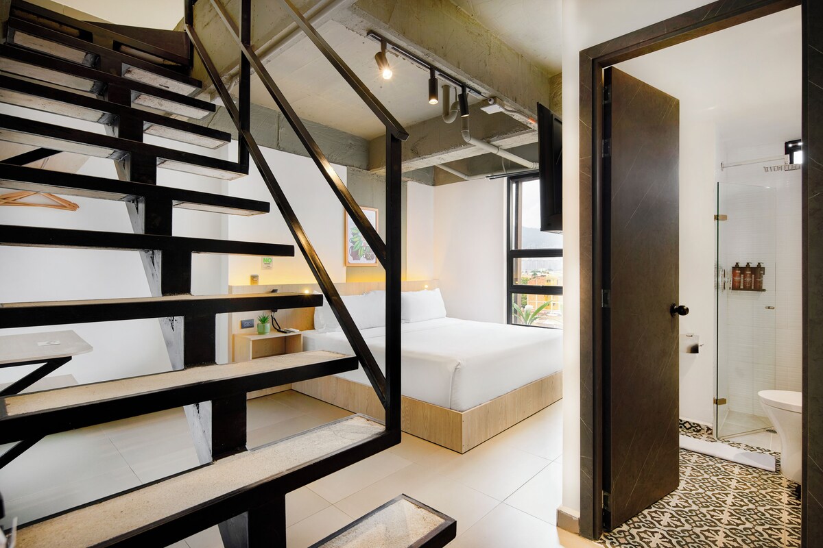 Un dormitorio moderno con una escalera de madera, una cama y un baño con ducha e inodoro.