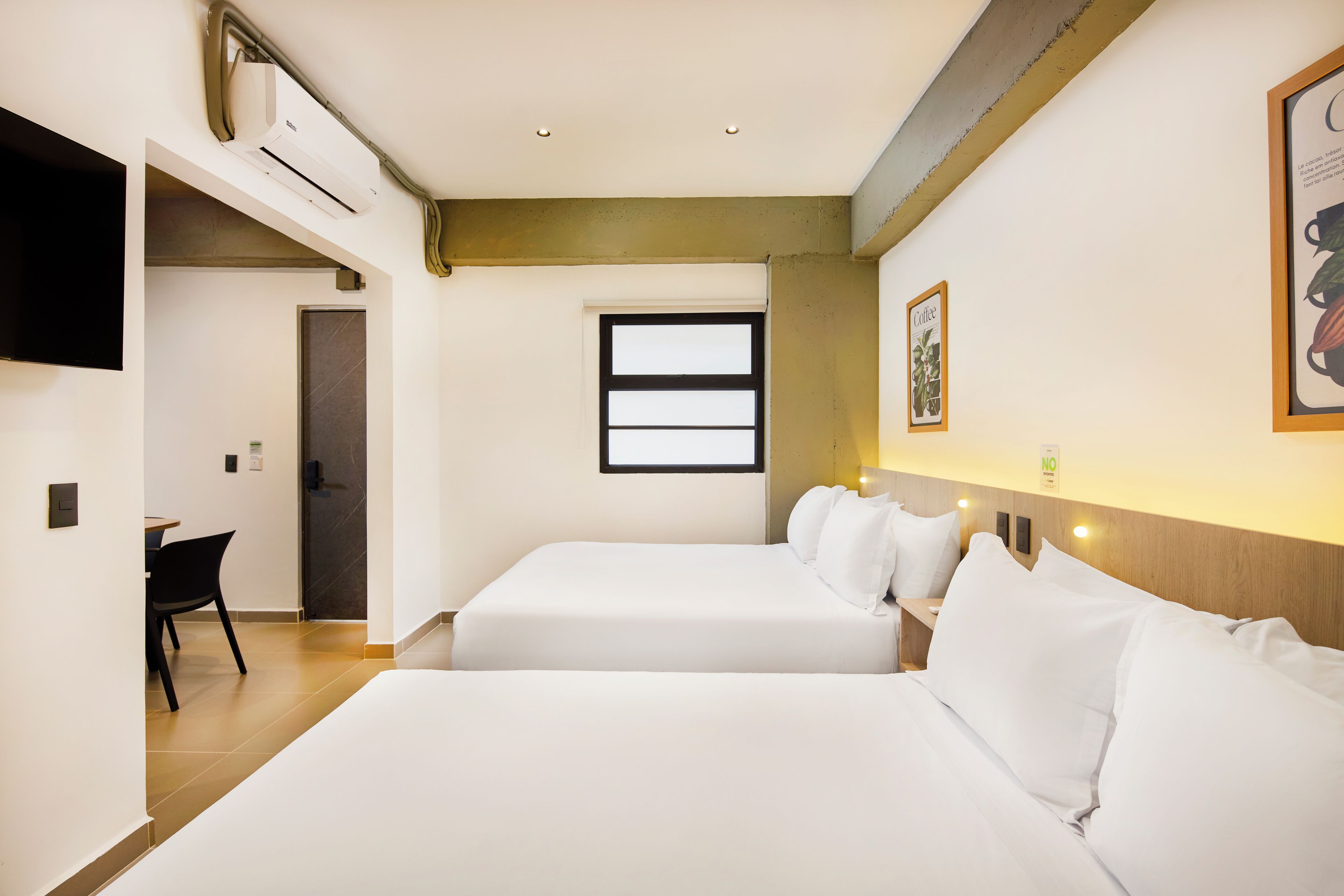 A hotel room with two beds, a desk, a chair, a TV, and a window.