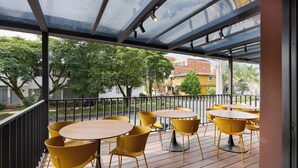 An outdoor patio with yellow chairs and tables, a glass ceiling, and a view of buildings and trees. - Hotel Attic 33 (Medellín)