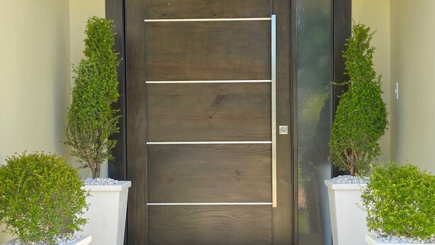 A modern entrance with a dark wooden door, white steps, and two potted plants on either side.