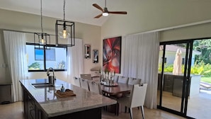 A modern kitchen with a central island, dining area with chairs, and a large window.