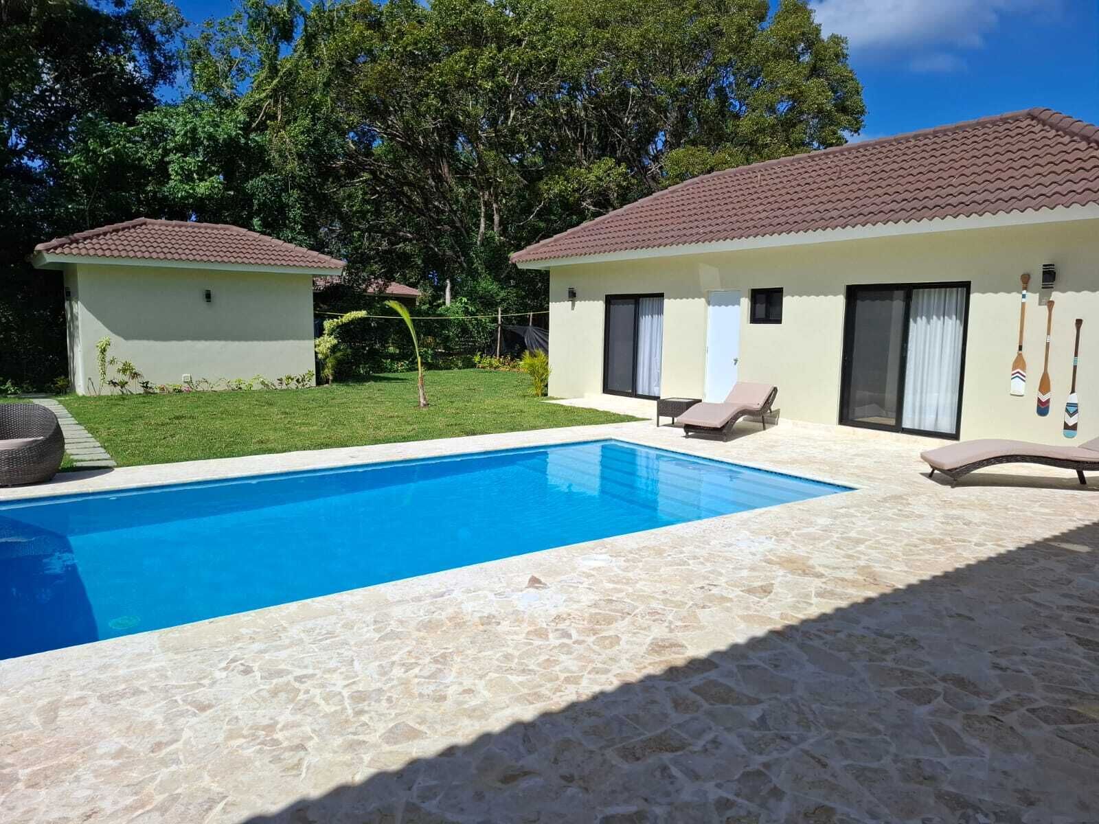 A swimming pool with lounge chairs, a small building, and a garden.