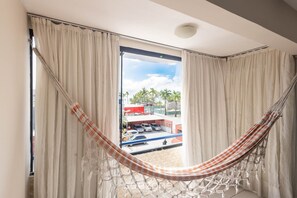 A room with a hammock, large windows, and a view of parked cars and palm trees outside.