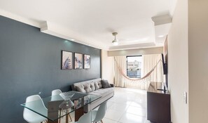 A modern living room with a glass dining table, grey sofa, and a hammock by the window. - 1-bedroom Apt 100 m From Jatiuca Beach Ber0202 (Maceió)