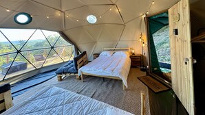 A cozy tented accommodation with a bed, seating area, and a view of the outdoors. - Bambou Dome - Cosy dome with panoramic mountain views, surrounded by beautiful nature (Riols)