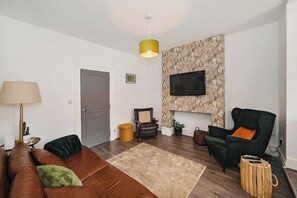 Ein Wohnzimmer mit einer Couch, Sesseln, einem Fernseher, einer Lampe und einer Wand mit Muster.
