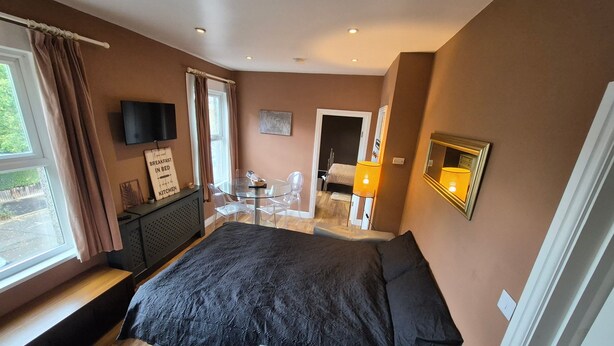 A bedroom with a large bed, a TV, a breakfast sign, a glass table, and a view of the outside. - Walk to East Croydon Station, 15 min direct train to Gatwick and Central London (Greater London)