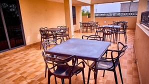 A covered outdoor dining area with multiple tables and chairs, a tiled floor, and a view of the surrounding area. - Monabliss Hotel and Suites  (Abakaliki)