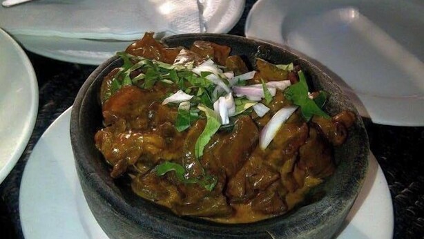 A bowl of curry with onions and green herbs on a white plate. - Monabliss Hotel and Suites  (Abakaliki)