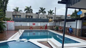 A swimming pool with a 'POOL RULES' sign, a 'NEW LABEL' sign, and a covered seating area with chairs. - Monabliss Hotel and Suites  (Abakaliki)