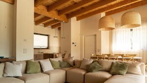 Un'ampia zona giorno con un grande divano componibile color beige, travi in legno a soffitto e due lampade a sospensione in rattan.