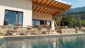 Una casa moderna con piscina, pareti in pietra e sedie a sdraio in legno.