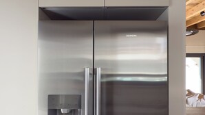 Un frigorifero Siemens in acciaio inossidabile con dispenser d'acqua, situato in una cucina moderna con mobili chiari e soffitto in legno.
