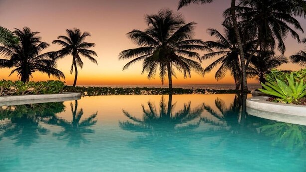 A pool with palm trees and a sunset view. - La Beliza Resort (San Pedro)