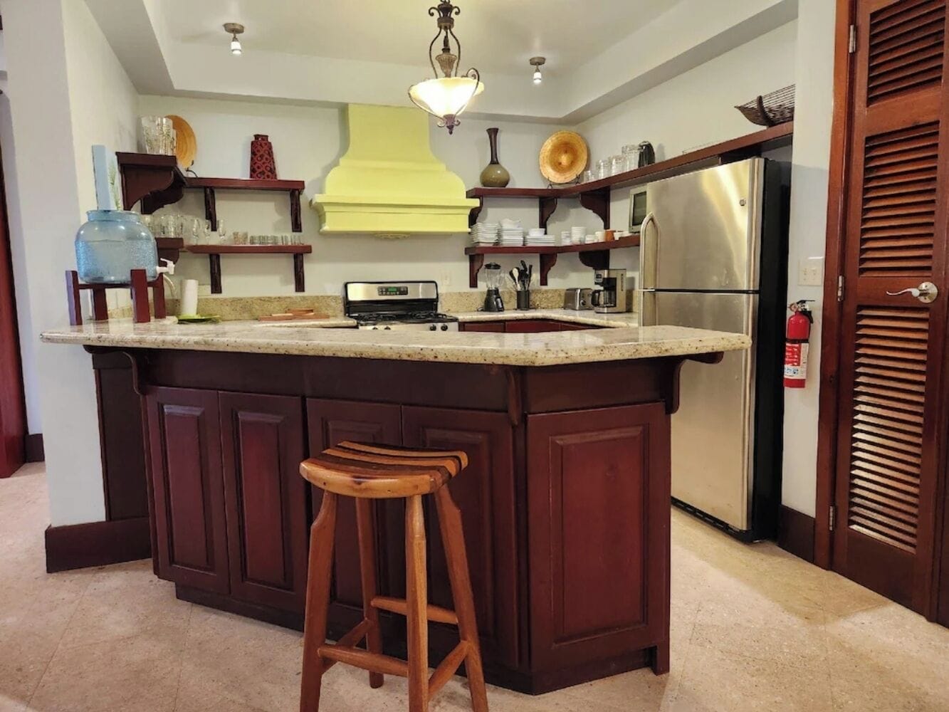 A kitchen with a central island, bar stools, a refrigerator, and various kitchen appliances.
