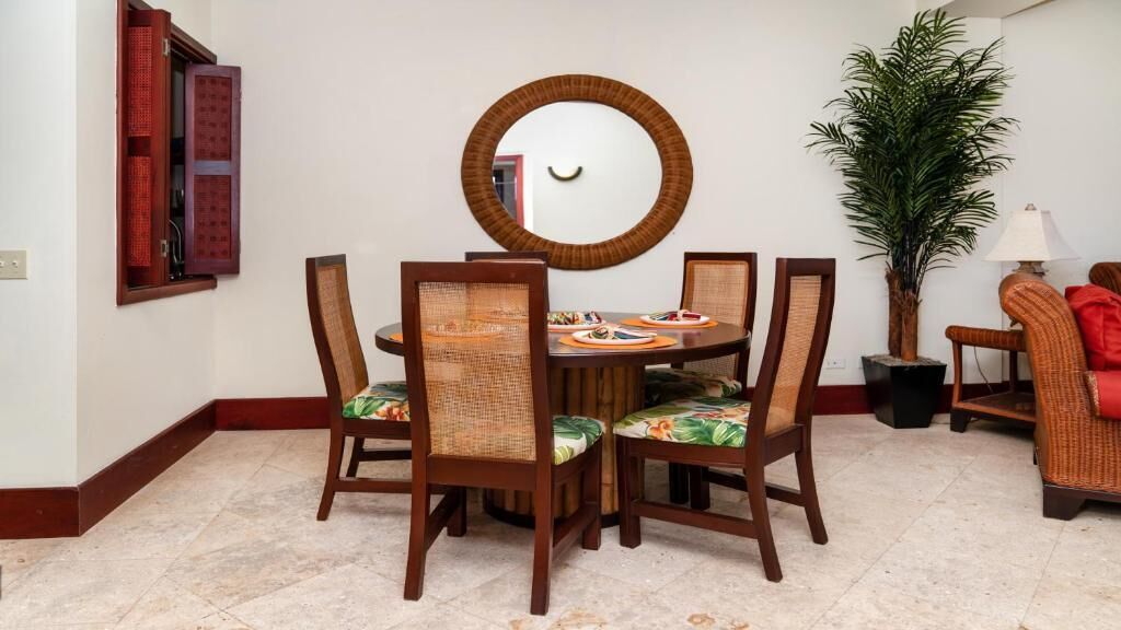 A dining area with a round table, six chairs, a mirror, a potted plant, and a red chair.