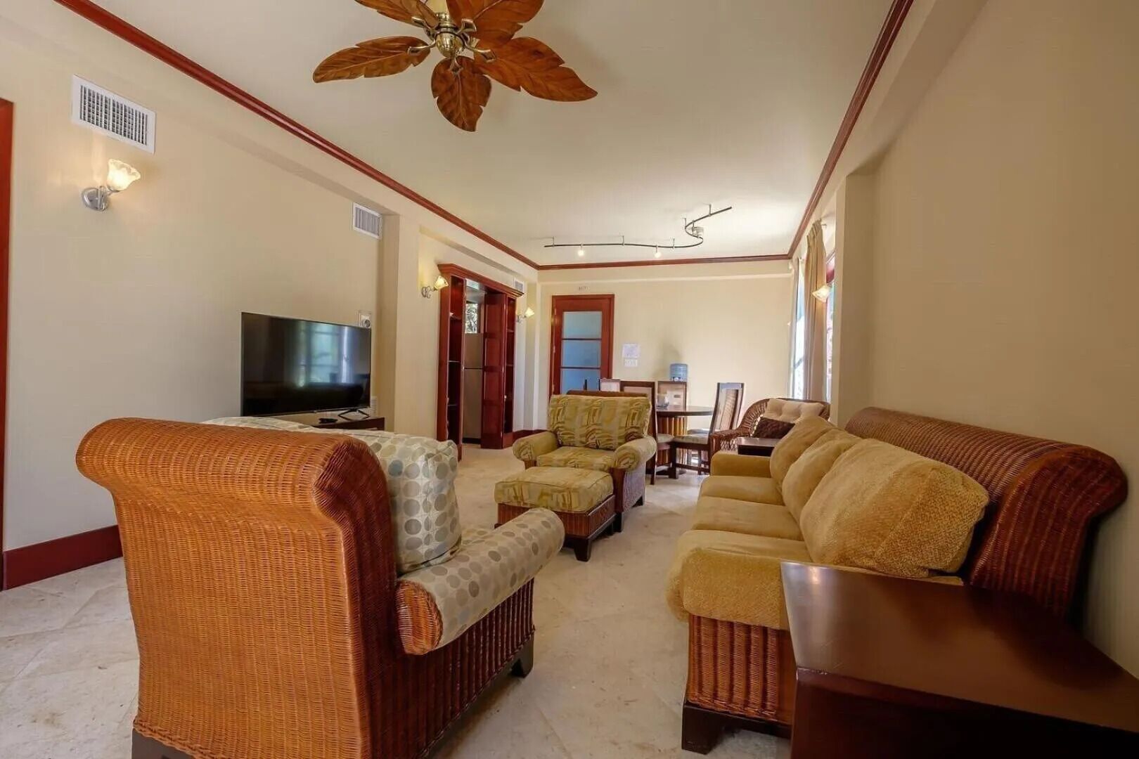 A living room with a television, wicker furniture, a ceiling fan, and a dining area in the background.
