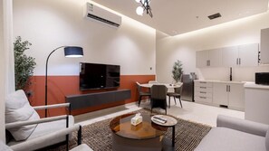 A modern living room with a flat-screen TV, a dining area, and a kitchenette.