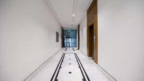 A modern hotel corridor with a clean, white floor and a wooden door on the right. - Super Luxury two Bedroom Al Narjis (Riyadh)