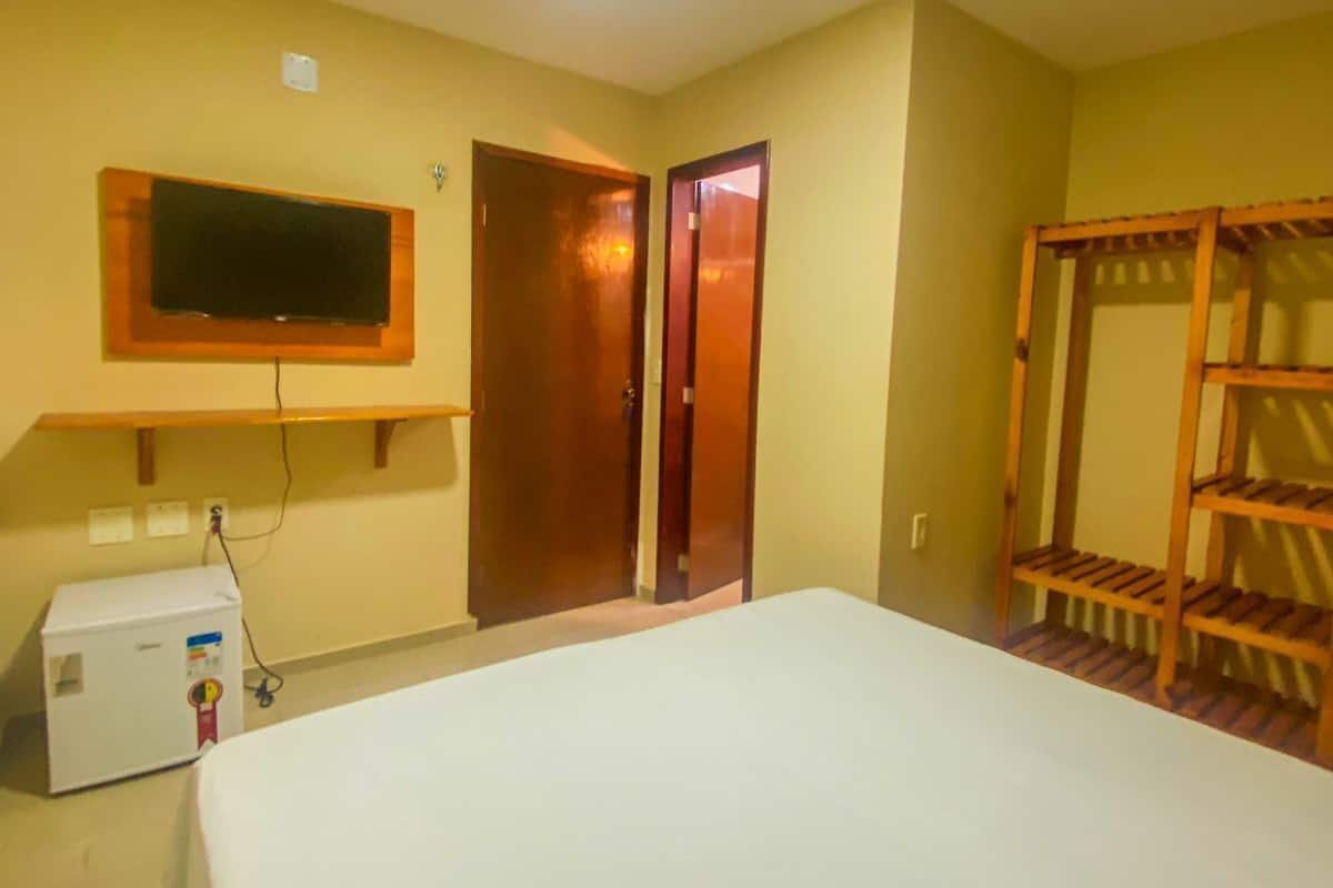 A hotel room with a bed, a television mounted on the wall, a wooden bunk bed, and a small desk with a computer.