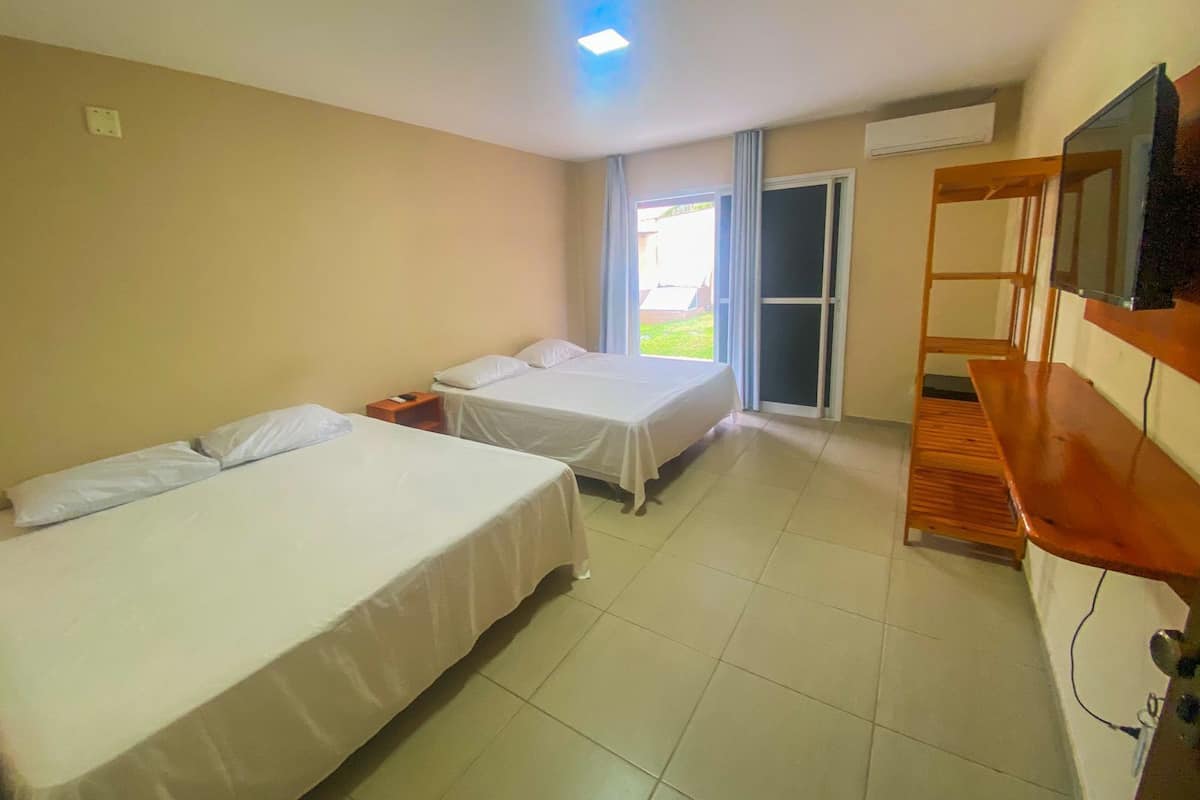 A hotel room with two beds, a wooden desk, a television, and a sliding glass door to the outside.