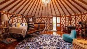 A spacious yurt interior with a bed, chandelier, and a patterned rug. - Luxury Yurt at Seaside Farm in Friendship (Friendship)