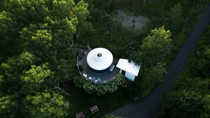 Vista aérea de un edificio circular rodeado de vegetación exuberante, con una carretera que conduce hacia él.