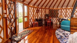 Interior de una yurta con paredes de celosía de madera, una zona de estar central con sillas, una mesita y un sofá azul.
