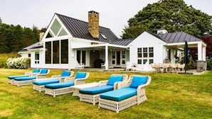A house with a covered porch, outdoor seating area with wicker furniture, and a stone chimney. - The Cottage at Seaside in Friendship (Friendship)