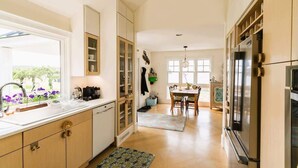 A modern kitchen with a large window, built-in cabinets, a refrigerator, and a dining area with a table and chairs. - The Cottage at Seaside in Friendship (Friendship)