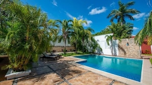 A swimming pool surrounded by palm trees and a stone wall, with lounge chairs and a tiled patio area. - Mérida Compound Stay – 2 Stays, 2 Double Rooms, Pool Access & Courtyard Views (Mérida)