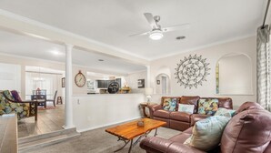 A spacious living room with a brown leather sofa, a wooden coffee table, and a dining area in the background.