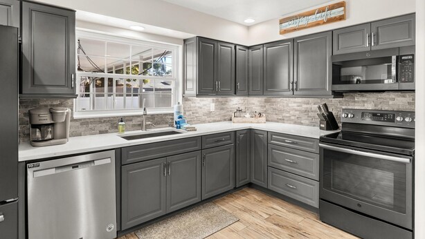 A modern kitchen with dark gray cabinets, a stainless steel dishwasher, a built-in oven, and a microwave.