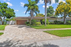 A residential house with a paved driveway, a garage, and a well-maintained lawn. - Clearwater Sanctuary Home w Pool (Clearwater)