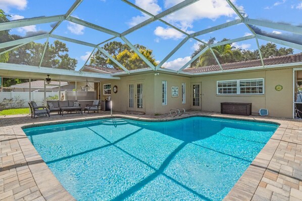 A swimming pool with a glass enclosure, surrounded by a patio area with outdoor furniture. - Clearwater Sanctuary Home w Pool (Clearwater)