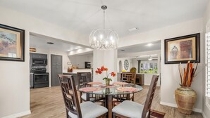 A modern dining area with a glass table, wooden chairs, and a chandelier.