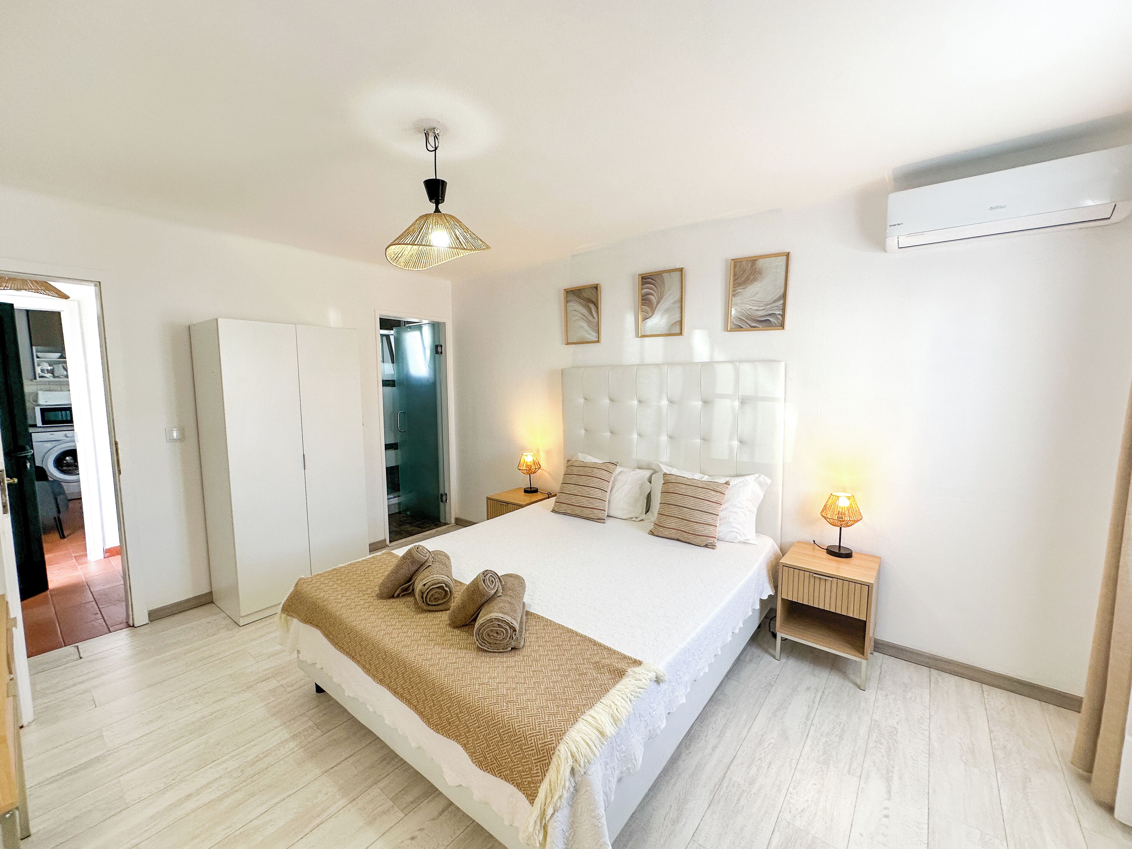 A hotel room with a large bed, a wardrobe, a bathroom with a glass door, and a ceiling fan.