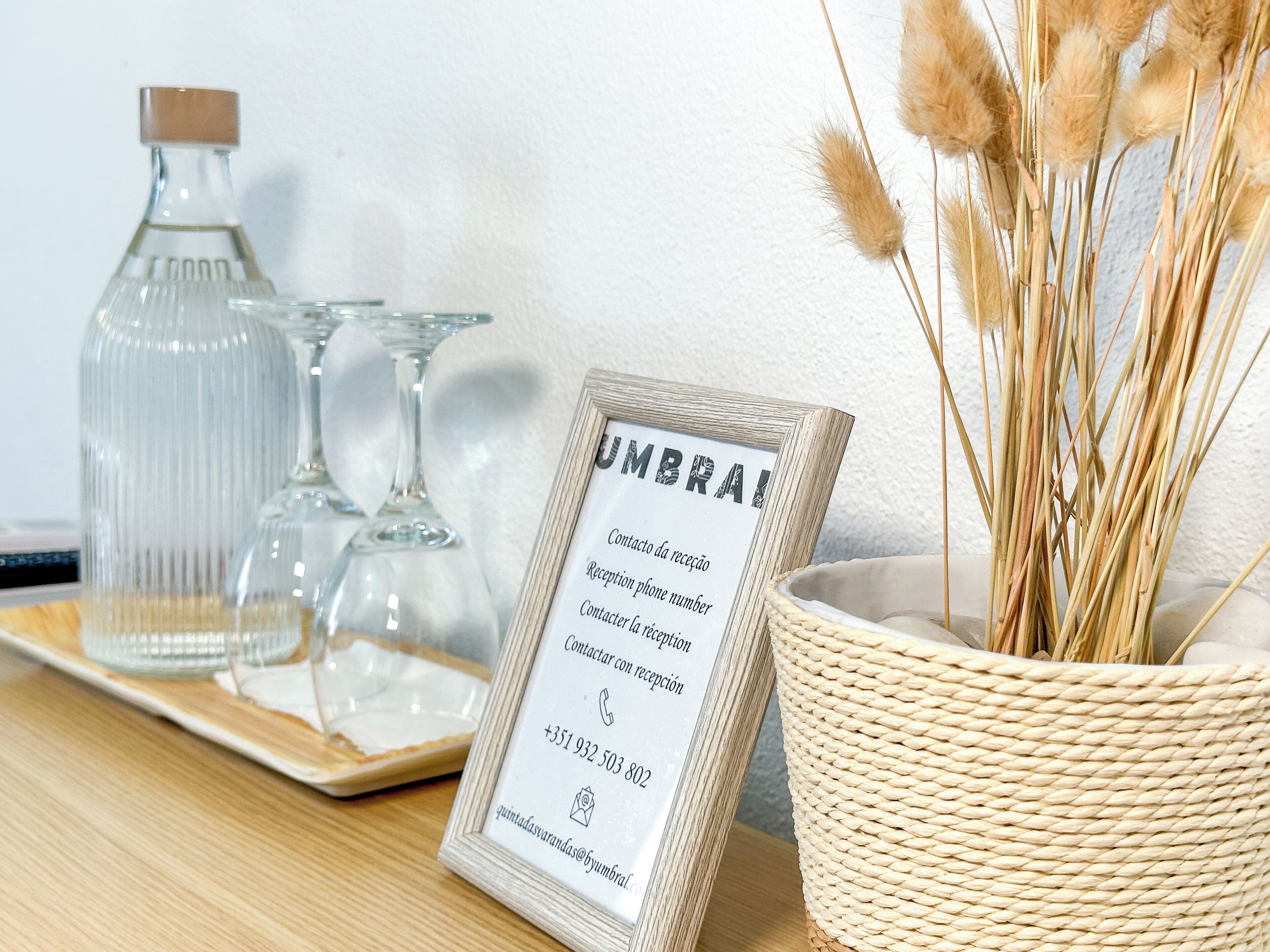 A reception desk with a framed sign listing reception details, a glass bottle, and a woven basket with dried plants.