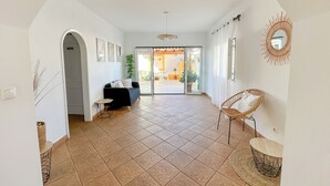 A spacious living area with a black sofa, a wicker chair, and a dining table. - Casa Alagoinha by Umbral (Odemira)