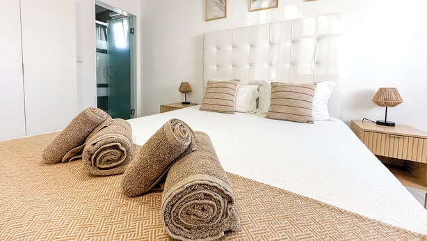 A neatly made bed with rolled towels, a tufted headboard, and a bedside lamp. - Casa Alagoinha by Umbral (Odemira)