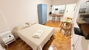 A compact bedroom with a bed, bedside table, and a wardrobe. Adjacent is a small kitchenette with a dining area. - Loft Copa Charm (Rio de Janeiro)