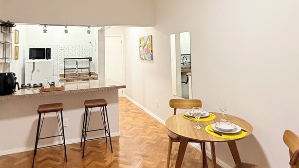 A spacious living area with a herringbone wood floor, a dining table with chairs, and a kitchen area in the background. - Loft Copa Charm (Rio de Janeiro)