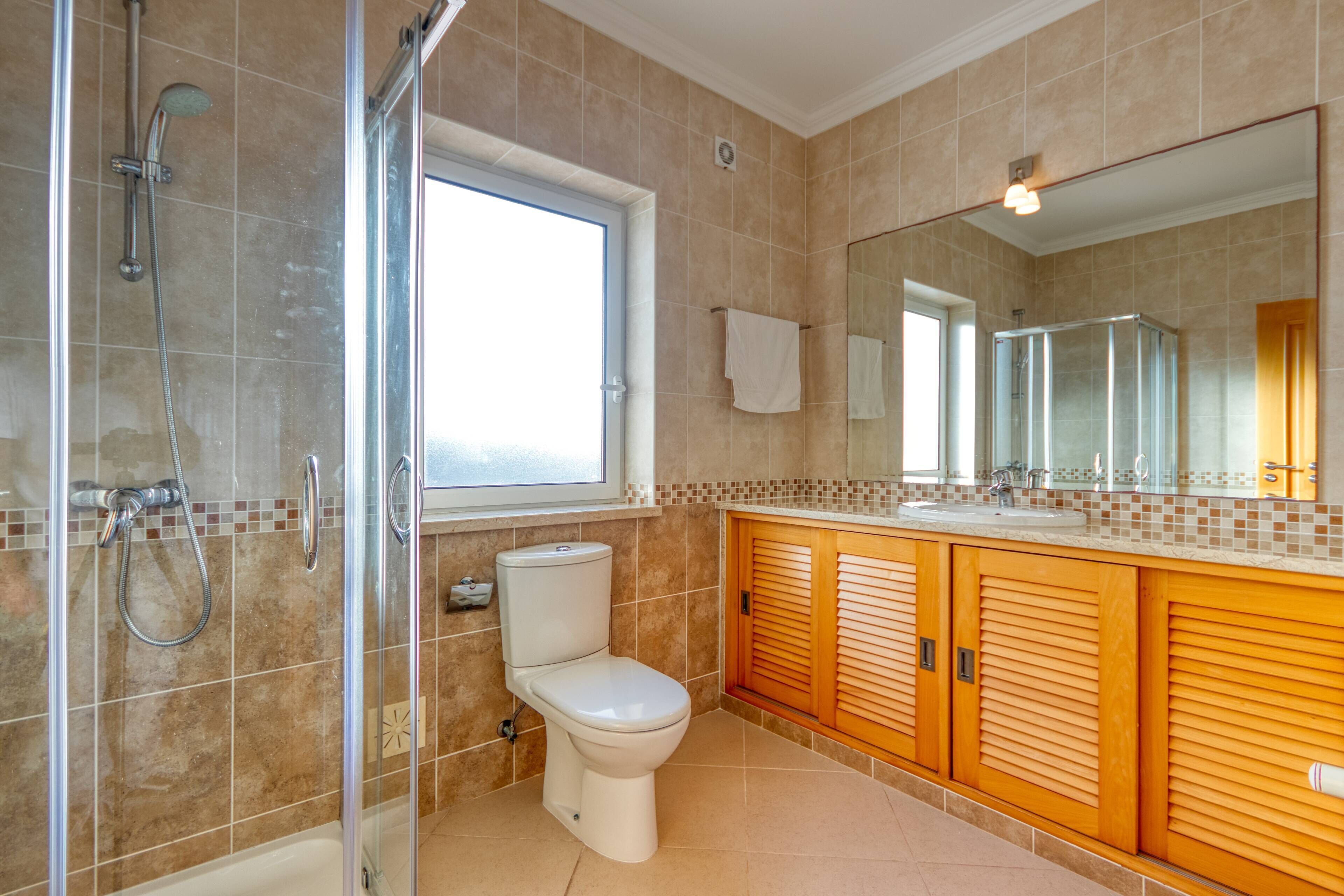 Ein Badezimmer mit Duschkabine aus Glas, Toilette und Waschtisch mit Spiegel.