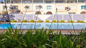 A swimming pool surrounded by lush greenery and a building with multiple balconies and arched windows.