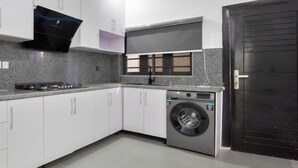 Uma cozinha moderna com armários brancos, fogão embutido, máquina de lavar e uma porta preta.