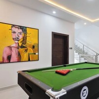 Una mesa de billar con taco y bolas, un cuadro en la pared y una escalera al fondo.