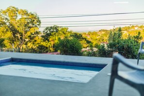 Piscina com borda em azulejo, rodeada por vegetação e céu limpo.