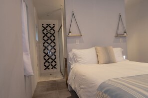 Quarto com cama, mesa de cabeceira, planta pendente e porta estampada.