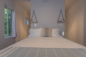 Un dormitorio con una cama grande, una ventana con cortinas y dos estantes en la pared con plantas en macetas.